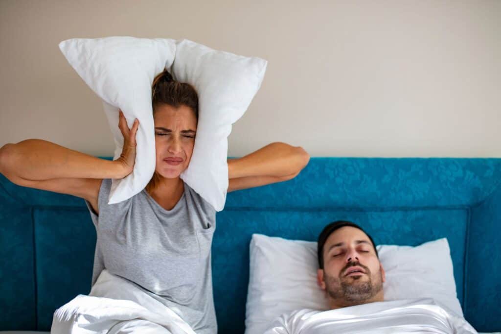 Woman covering her ears with a pillow while her partner snores