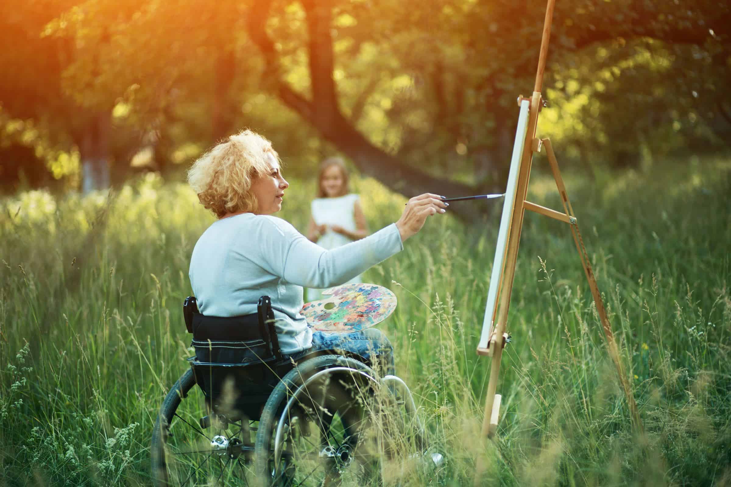 Woman in a wheelchair painting at an easel outdoors