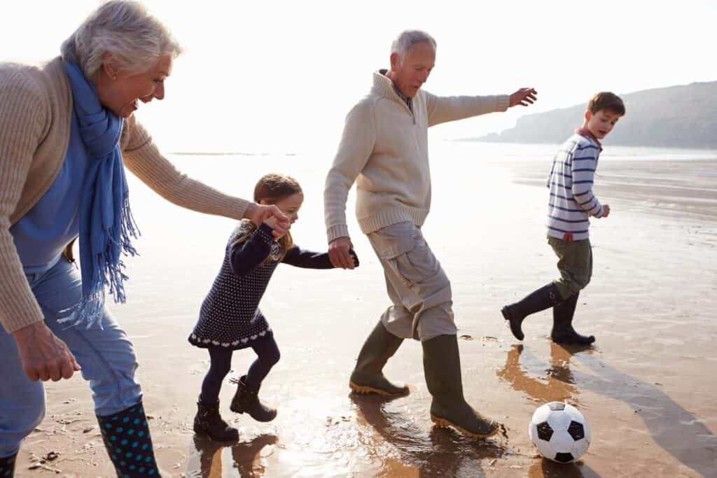 Grandparents playing football on the beach with a child